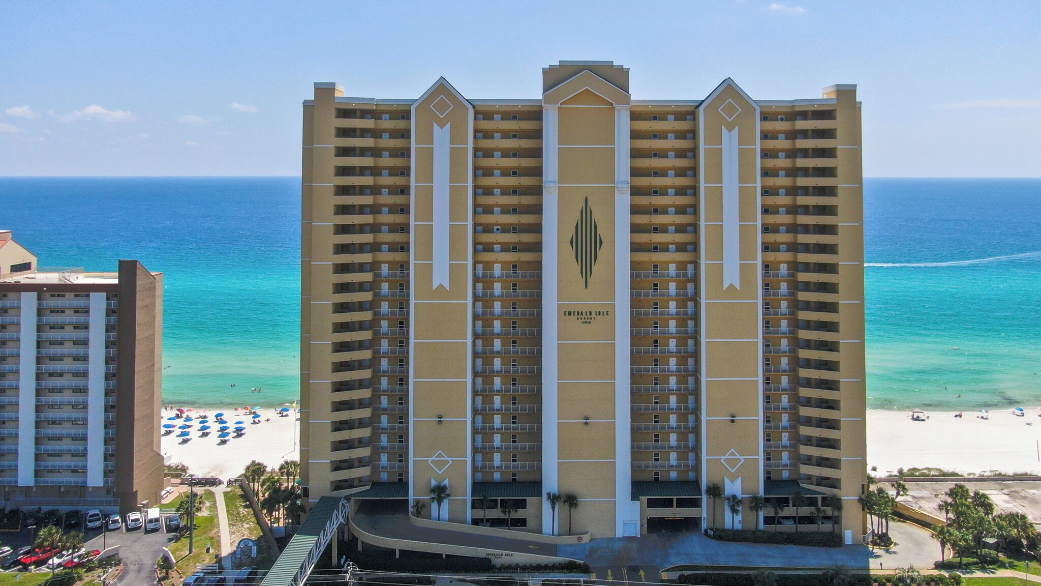 A high-rise hotel with multiple balconies, a beach view, and a parking area.