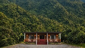 A lodge with a wooden exterior, a porch with chairs, and a view of a forested mountain.