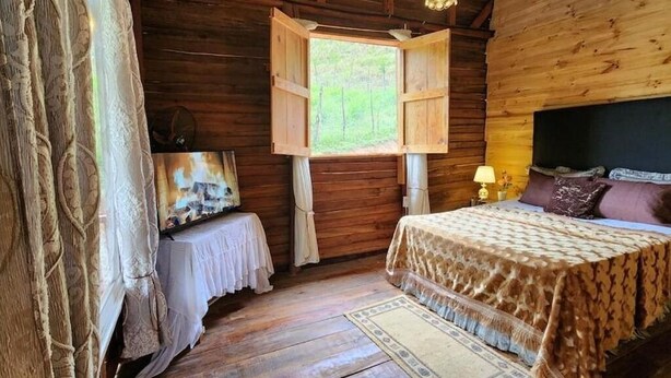 A wooden cabin bedroom with a bed, a window, a lamp, and a painting on the wall.