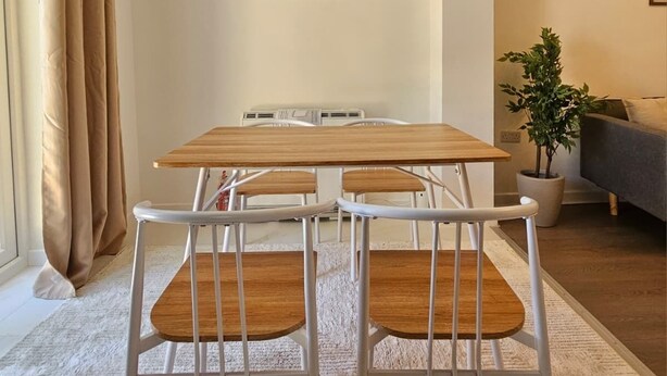 A modern living room with a wooden dining table and chairs, a potted plant, and a painting on the wall. - Luxury 2Bedroom Near Station + Bike (Cambridge)