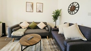 A living room with two sofas, a coffee table, and a wall clock. - Luxury 2Bedroom Near Station + Bike (Cambridge)