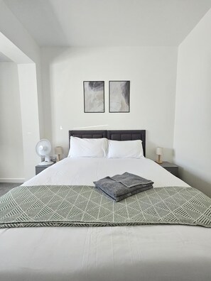 Ein ordentlich bezogenes Bett mit einer Decke im geometrischen Muster, ein Nachttisch mit einer Lampe und zwei abstrakte Gemälde an der Wand.