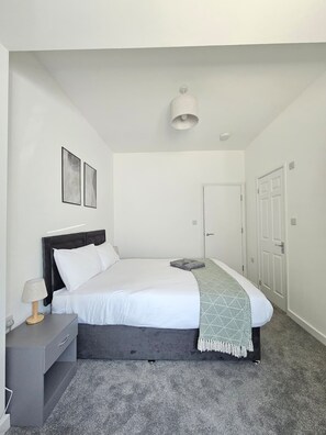 A bedroom with a bed, bedside table, lamp, and a door. - Luxury 2Bedroom Near Station + Bike (Cambridge)