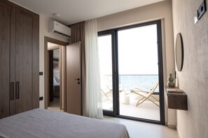 A bedroom with a bed, a wardrobe, a sliding glass door to a balcony, and a view of the sea. - Strovilla Gaia 3 Luxury Private Beachfront Villas (Psakoudia)