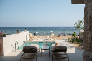 A poolside area with lounge chairs, a table, and a view of the beach and sea. - Strovilla Gaia 3 Luxury Private Beachfront Villas (Psakoudia)