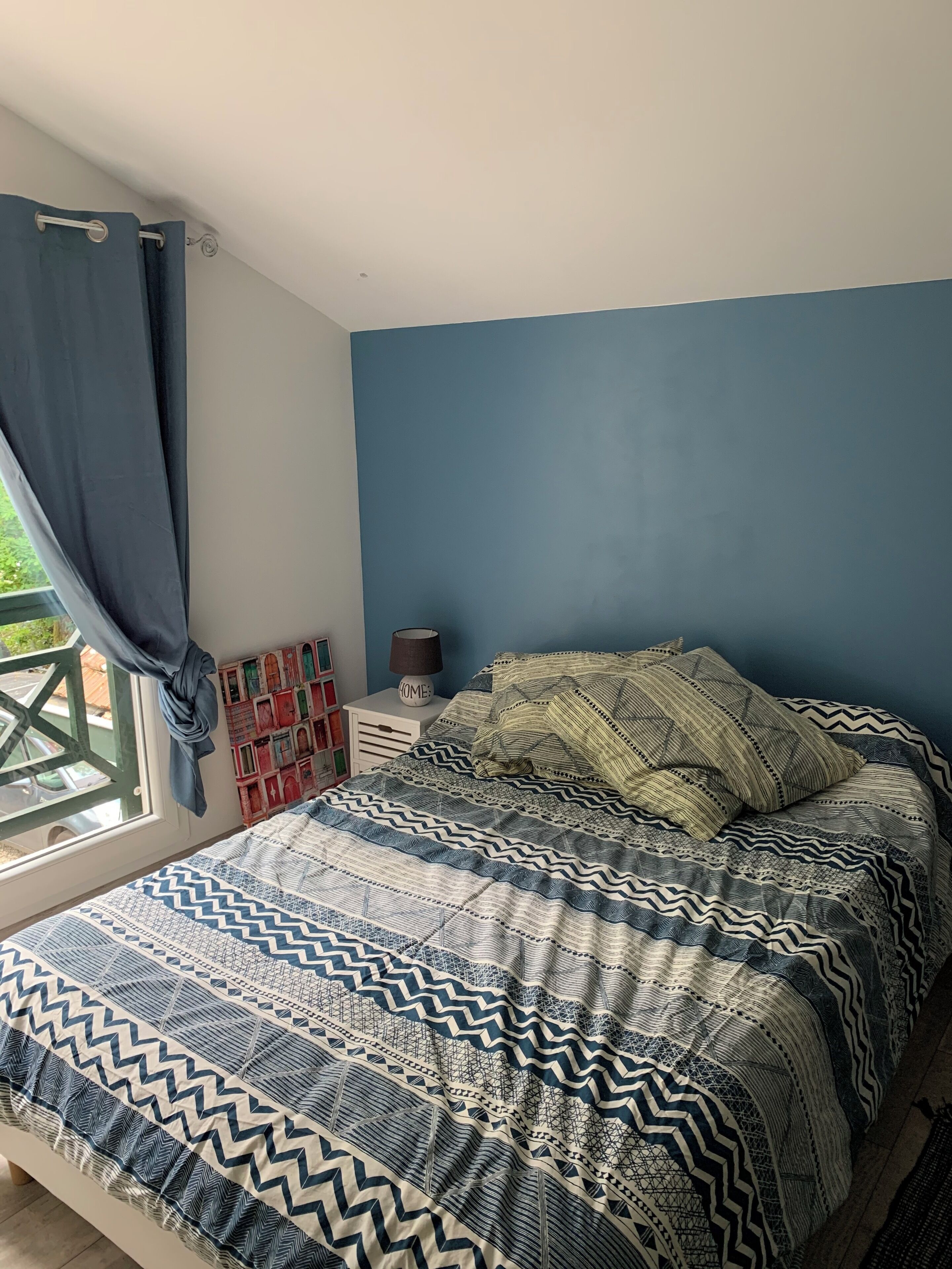 Un dormitorio con cama, mesita de noche, lámpara y ventana con cortinas.