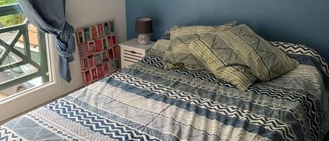 Un dormitorio con cama, mesita de noche, lámpara y ventana con cortinas.