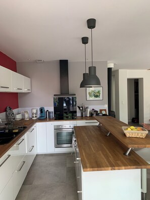 A modern kitchen with white cabinetry, a wooden countertop, a built-in oven, and a large island with a basket of fruit. - Abatilles-Arcachonnaise, 10-person capacity - Near the beach and shops (Arcachon)