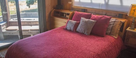 A bedroom with a large bed, a nightstand, a lamp, and a view of the outdoors.