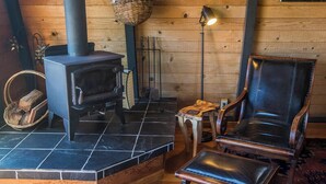 A cozy room with a wood-burning stove, a leather armchair, and a small table with a lamp. - Moon Shadow (TOT ID #2164): 2  BR, 2  BA House in The Sea Ranch, Sleeps 4 (The Sea Ranch)