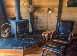 A cozy room with a wood-burning stove, a leather armchair, and a small table with a lamp. - Moon Shadow (TOT ID #2164): 2  BR, 2  BA House in The Sea Ranch, Sleeps 4 (The Sea Ranch)