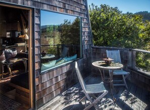 A wooden deck with a glass door leading to a room, outdoor seating, and a view of greenery. - Moon Shadow (TOT ID #2164): 2  BR, 2  BA House in The Sea Ranch, Sleeps 4 (The Sea Ranch)