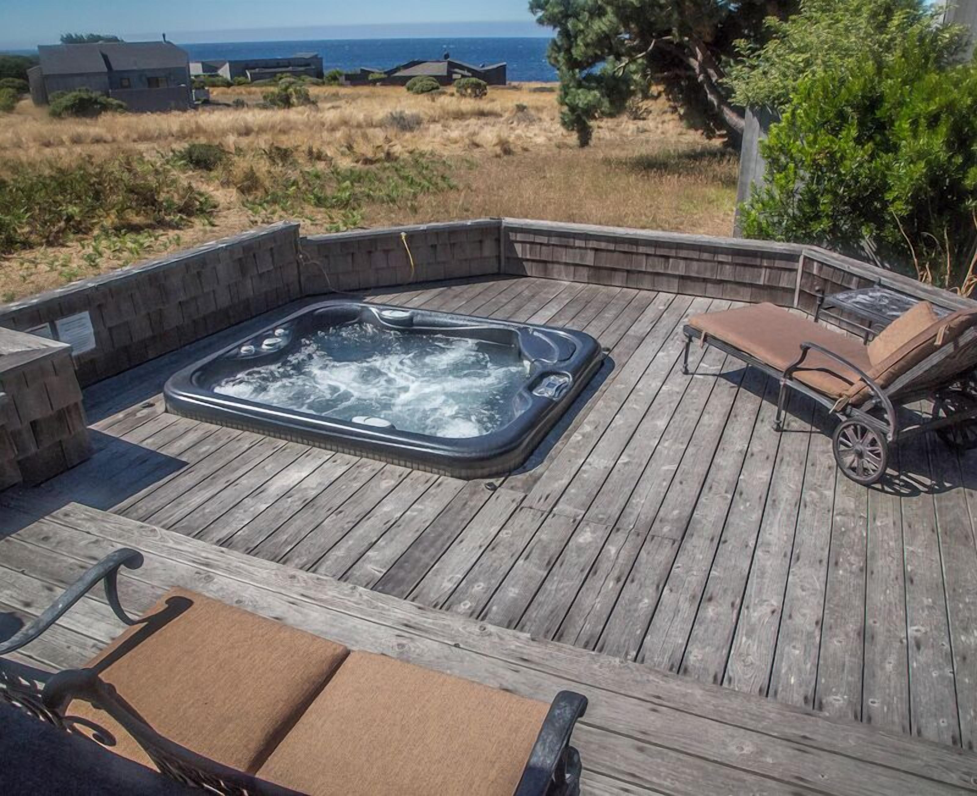 Un patio in legno con una vasca idromassaggio, poltrone relax e vista sull'oceano.