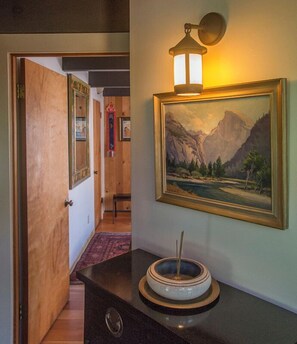 A hallway with a framed landscape painting, a wall-mounted light fixture, and a decorative bowl on a dark countertop. - Moon Shadow (TOT ID #2164): 2  BR, 2  BA House in The Sea Ranch, Sleeps 4 (The Sea Ranch)