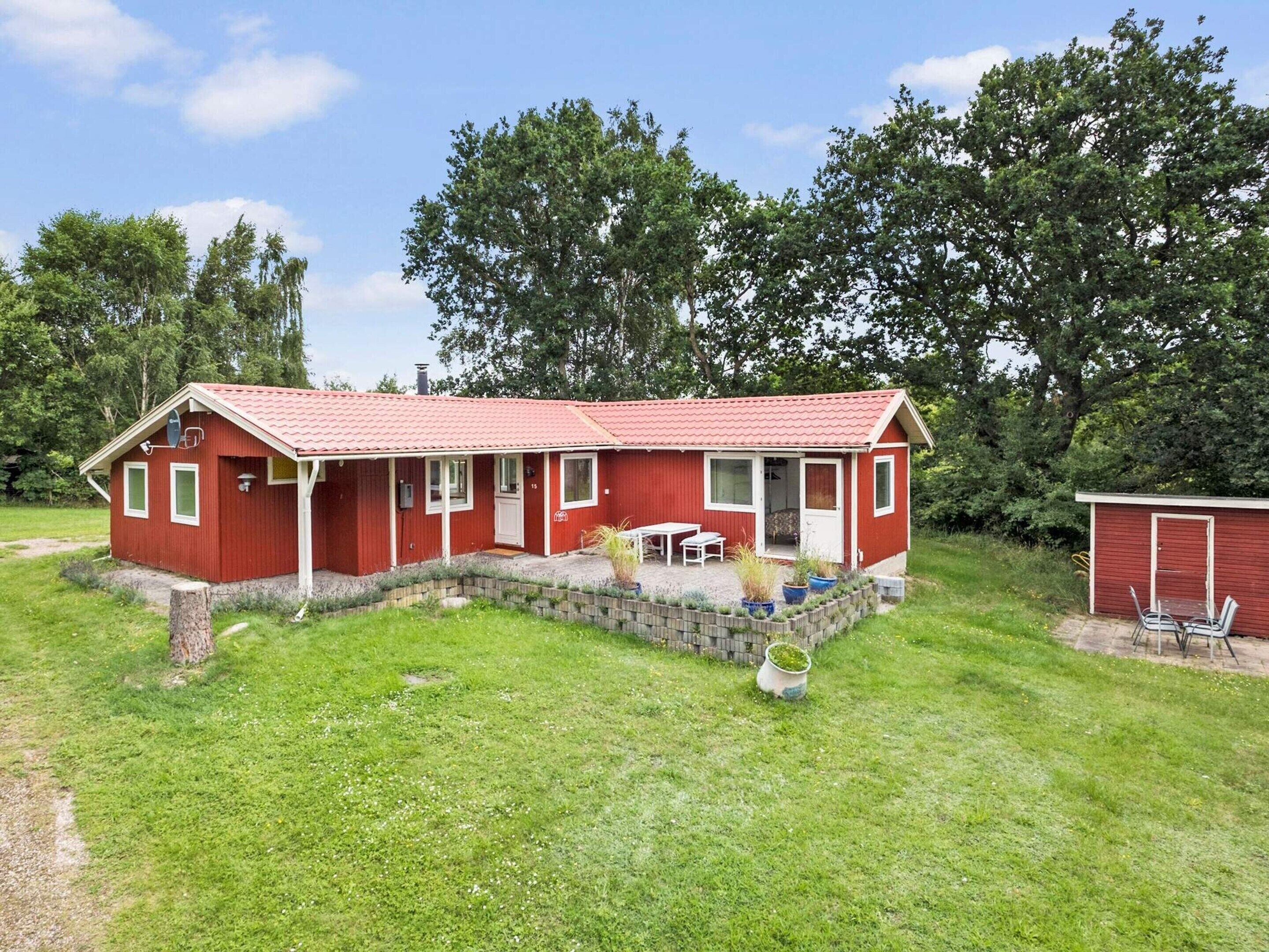 A red single-story house with a tiled roof, a front porch, and a small garden area with potted plants.