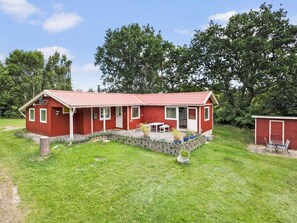 A red single-story house with a tiled roof, a front porch, and a small garden area with potted plants. - 5 Star Holiday Home in Jaegerspris (Jægerspris)