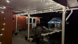 A covered outdoor area with a wooden structure, potted plants, and a greenhouse. - 5 Star Holiday Home in Jaegerspris (Jægerspris)