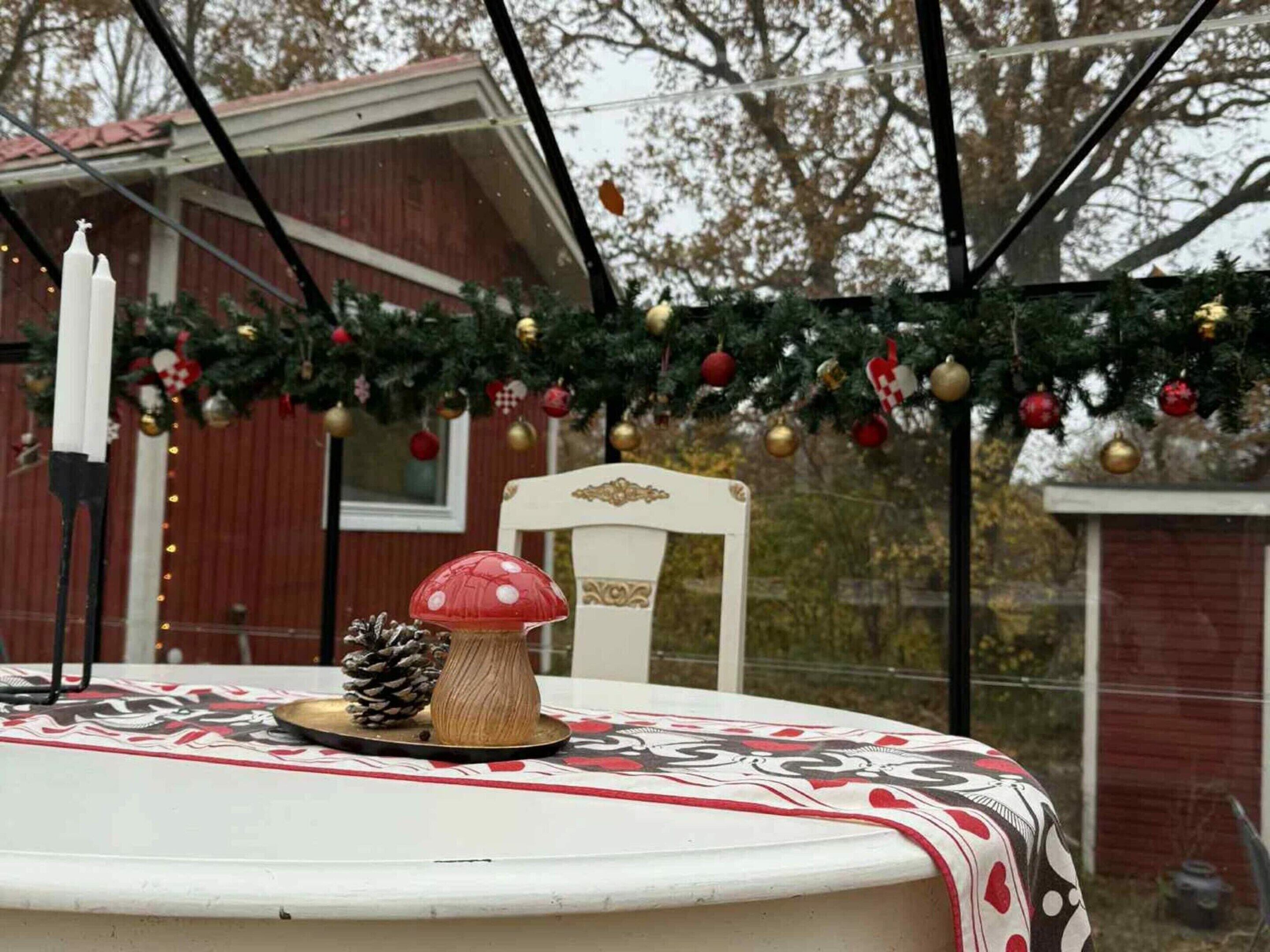 A table with a patterned tablecloth, a pine cone, and a decorative item on a porch with a Christmas tree in the background.