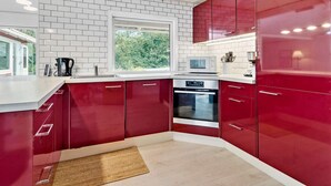 A modern kitchen with red cabinets, a built-in oven, and a window providing natural light. - 5 Star Holiday Home in Jaegerspris (Jægerspris)