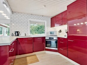 A modern kitchen with red cabinets, a built-in oven, and a window providing natural light. - 5 Star Holiday Home in Jaegerspris (Jægerspris)