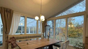 A dining area with a wooden table, white chairs, a bench, and a view through large windows. - 5 Star Holiday Home in Jaegerspris (Jægerspris)