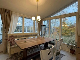 Un comedor con una mesa de madera, sillas blancas, un banco y vistas amplias a través de grandes ventanales.