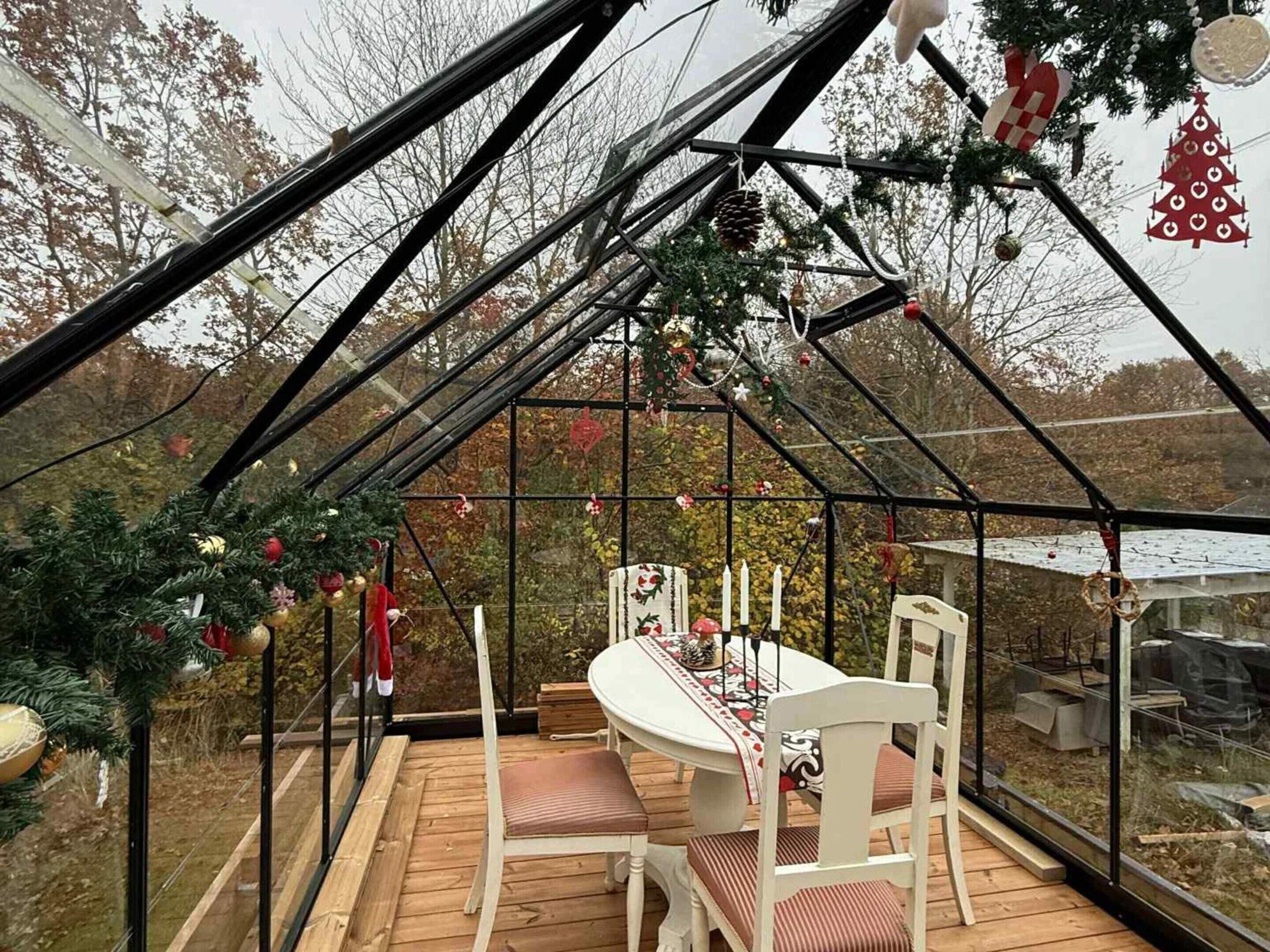 A greenhouse with a dining table and chairs, surrounded by Christmas decorations.
