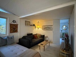 Una sala de estar con sofá, una mesa de centro y una cama. Hay una ventana con vistas a árboles.