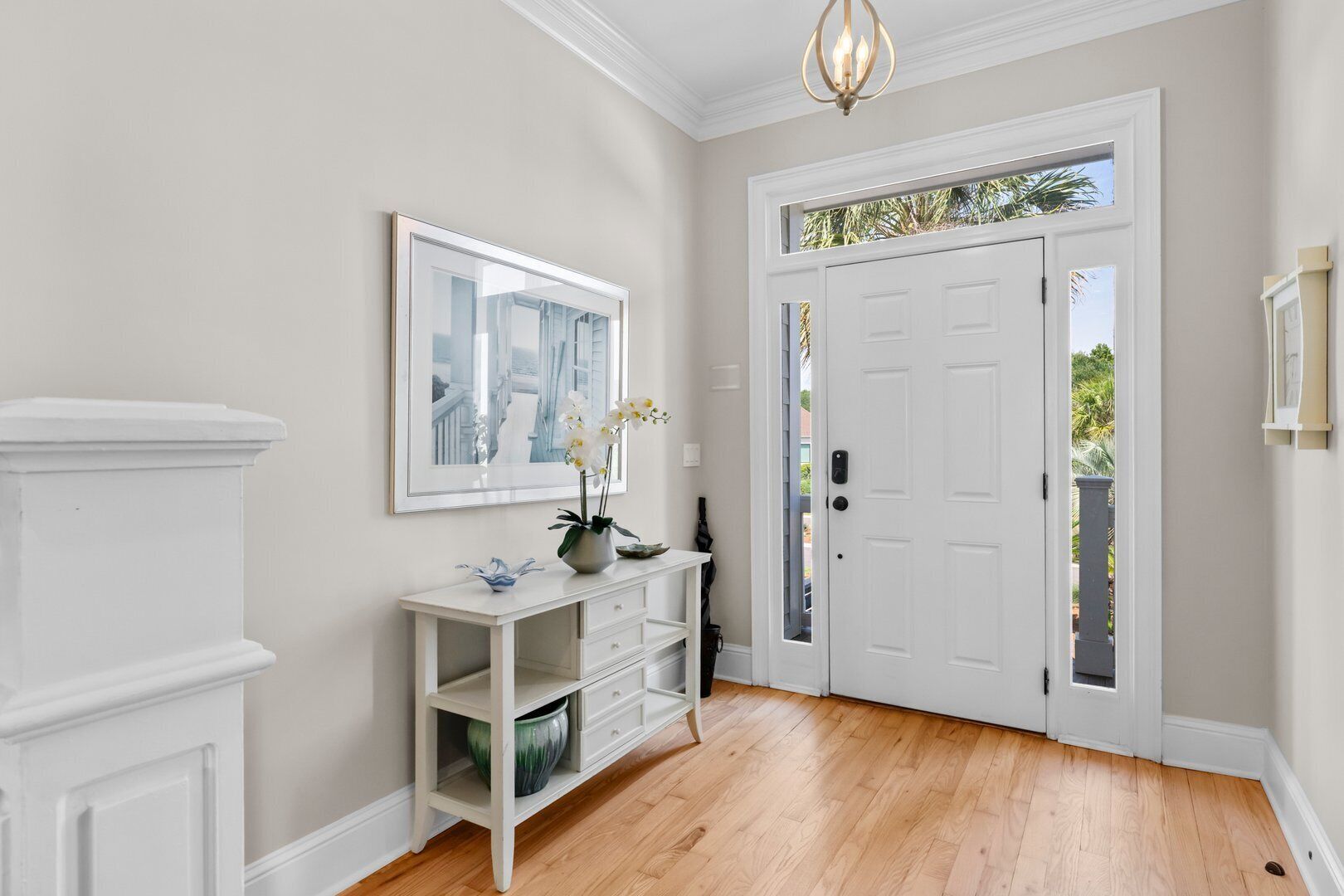 A hallway with a white door, a framed picture on the wall, a white console table with decorative items, and a wooden floor.
