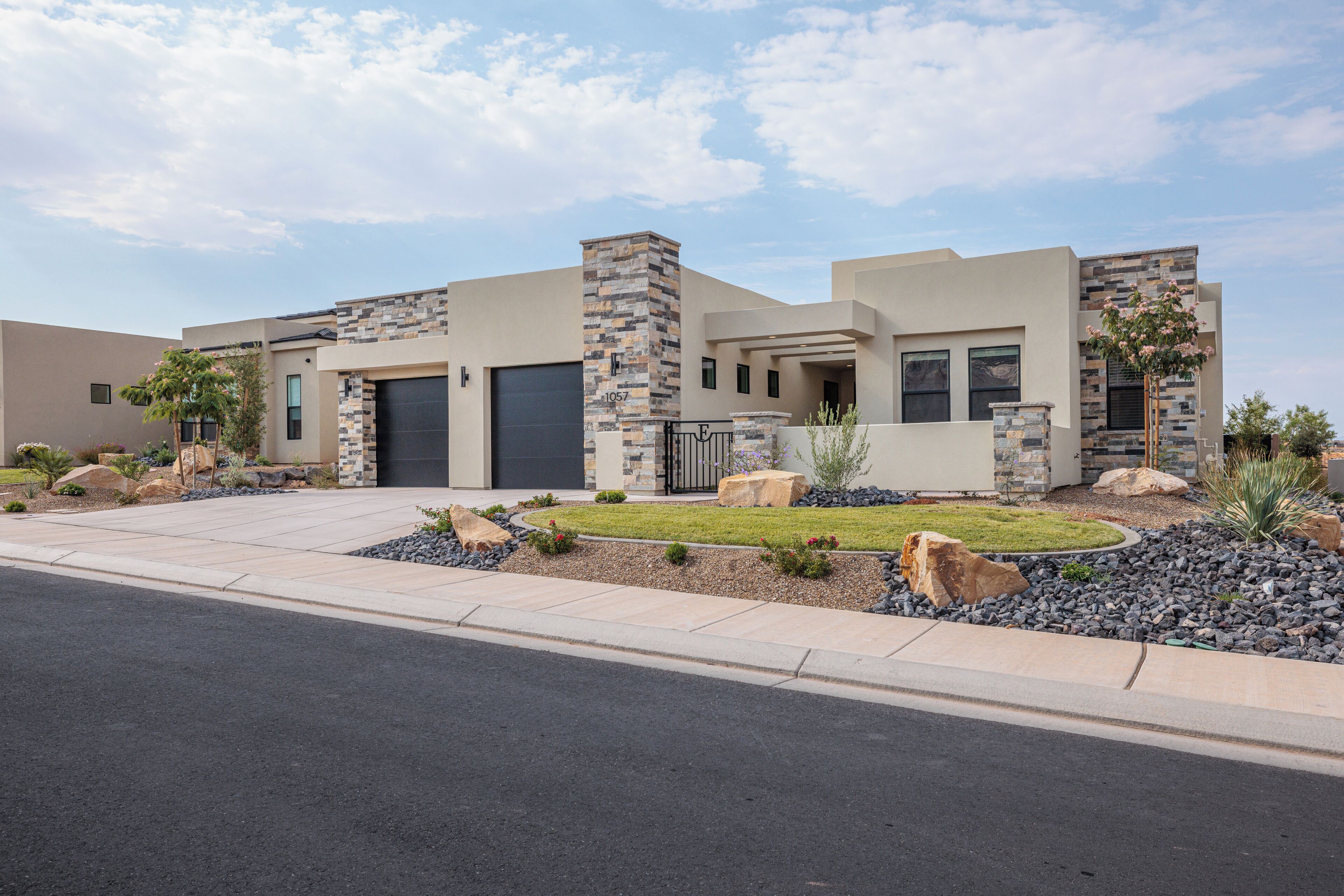 A modern two-story house with a stone facade, a garage, and a landscaped front yard with rocks and shrubs.