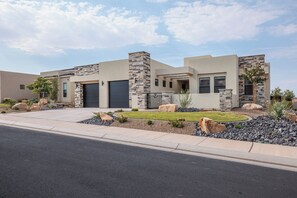 A modern two-story house with a stone facade, a garage, and a landscaped front yard with rocks and shrubs. - Serenity on the 6th: 4 BR, 4 BA House in St. George, Sleeps 10 (St. George)