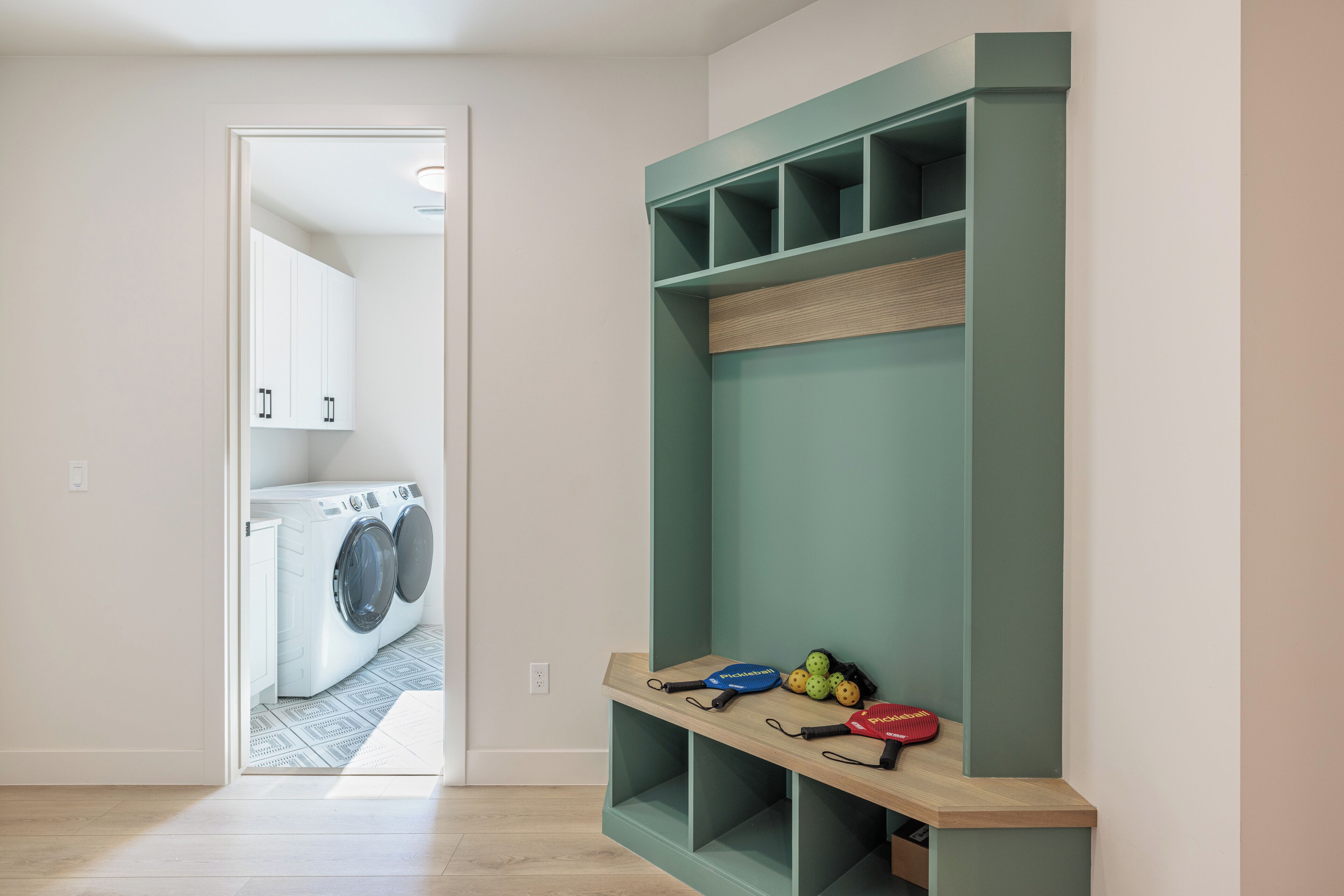 A laundry room with a washing machine, a shelf with sports equipment, and a door leading to another room.