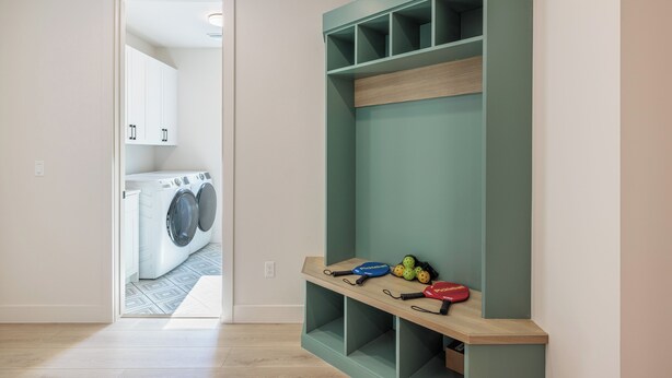 Een wasruimte met een wasmachine, een plank met sportattributen en een deur naar een andere kamer.