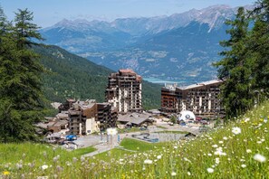 Ein kurvenreiches Urlaubsgebiet mit mehreren Gebäuden, darunter ein markantes, kuppelförmiges Bauwerk, umgeben von üppiger Vegetation und Bergen im Hintergrund.