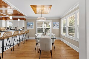 A dining area with a glass table, white chairs, and a wooden ceiling. - 🌊Sandman by the Sea - Pet Friendly 4 Bedroom Home with Spacious Decks🏖️ (Kure Beach)