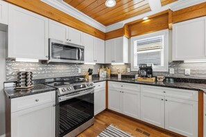 A modern kitchen with white cabinets, a stainless steel range, a microwave, and a coffee maker. - 🌊Sandman by the Sea - Pet Friendly 4 Bedroom Home with Spacious Decks🏖️ (Kure Beach)