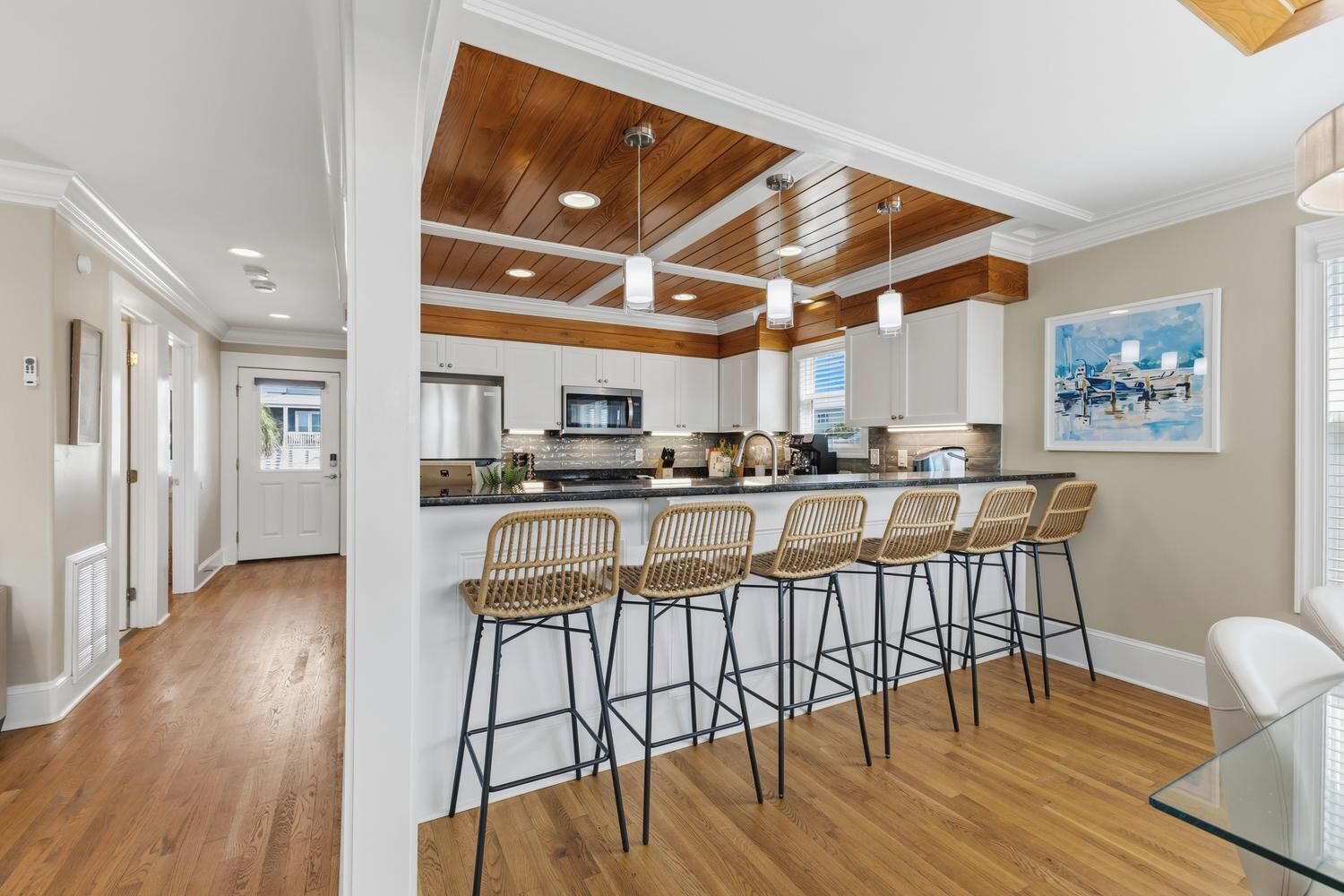 A modern kitchen with wooden ceiling beams, white cabinets, and a central island with bar stools.