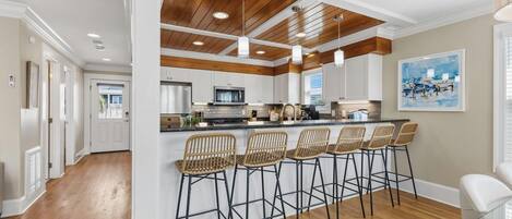 A modern kitchen with wooden ceiling beams, white cabinets, and a central island with bar stools.
