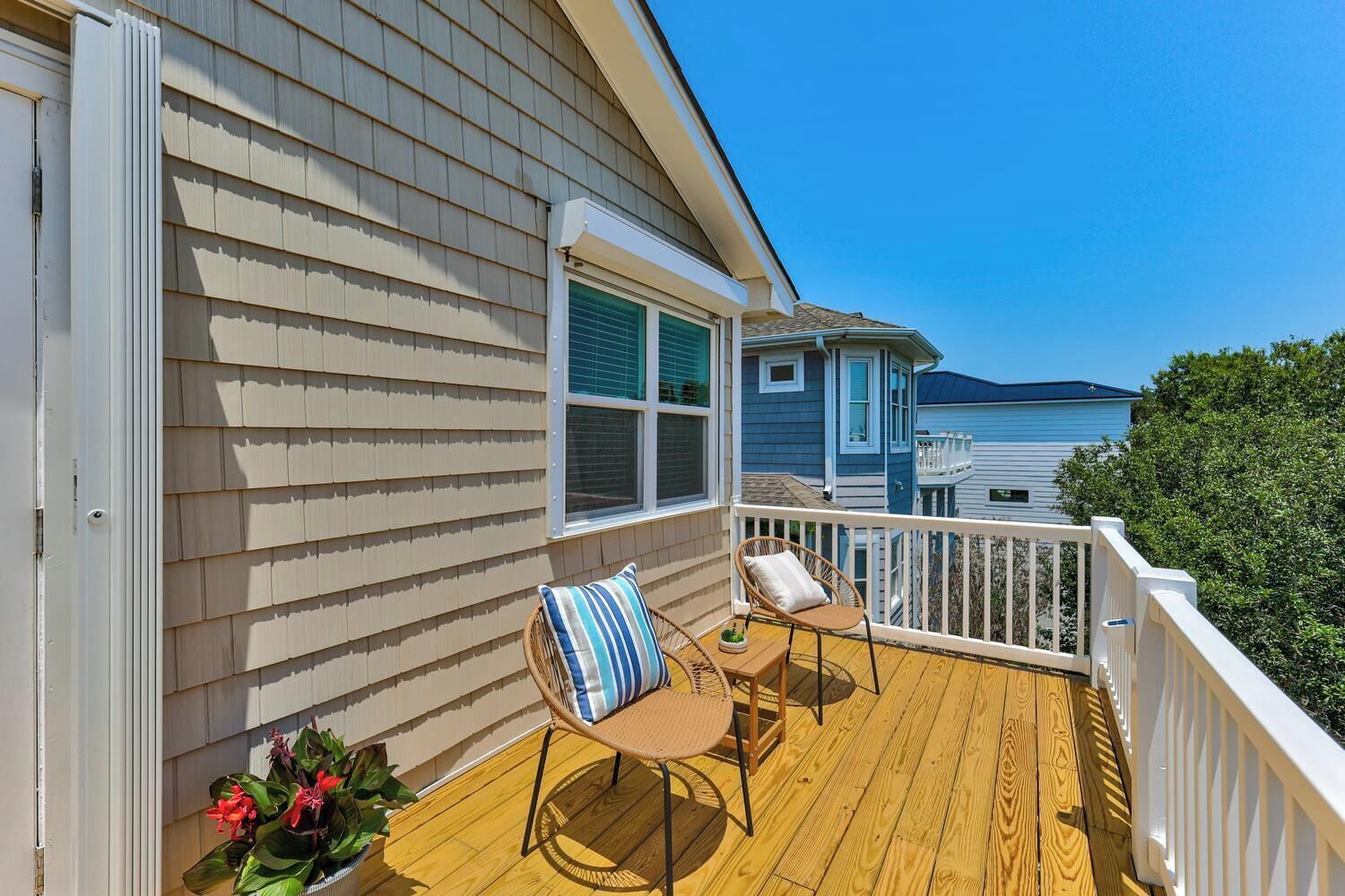 A wooden deck with two wicker chairs and a table, a white railing, and a window with shutters.
