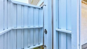 Une barrière métallique bleu clair, dotée d’un loquet, qui mène à un bâtiment à la façade beige.