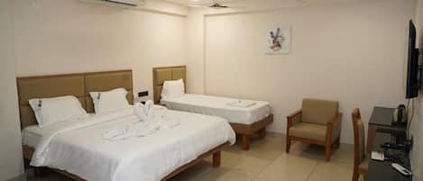 A hotel room with two single beds, a sofa, a desk with a television, and an air conditioning unit.