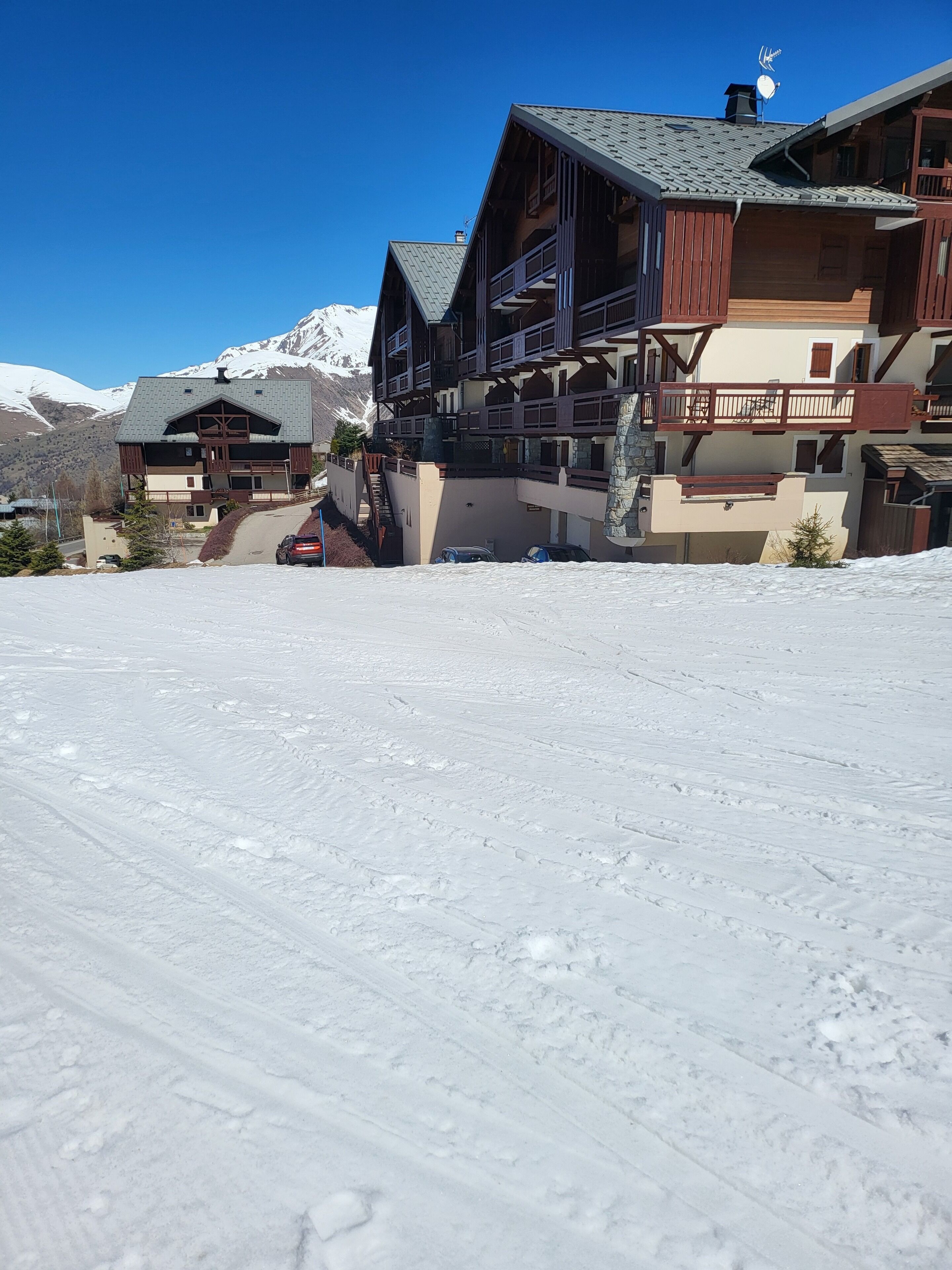 A multi-story lodge with a ski lift, snow-covered ground, and mountains in the background.