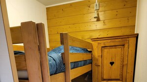 Ein Stockbett mit einer Holzleiter, ein kleines Schränkchen mit herzförmigem Griff und ein Fliesenboden.