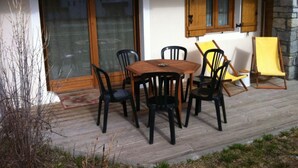 Eine Terrasse im Freien mit einem Holztisch und -stühlen, einem gelben Stuhl und einer Steinmauer.