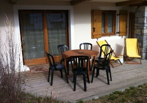 An outdoor patio with a wooden table and chairs, a yellow chair, and a stone wall. - 3-star apartment at the base of the slopes, large terrace, 2 bedrooms (Les Deux Alpes)