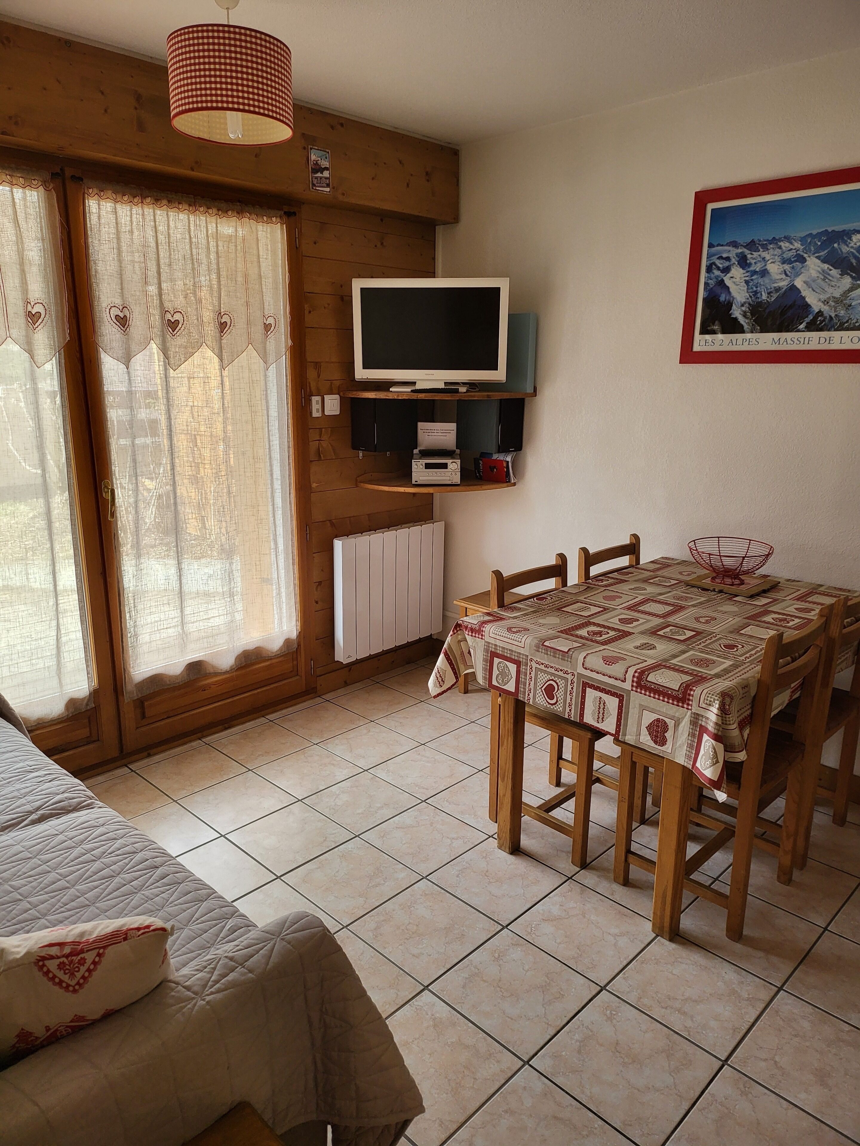 Een gezellige kamer met houten inrichting, een eettafel met stoelen, een televisie op een plank en een raam met gordijnen.