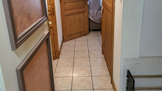 Ein Flur mit gefliestem Boden, Holztüren und einem Telefon an der Wand.