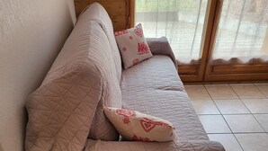Ein raumförmiger Raum mit Holzbalken, einer beigen Couch, einem kleinen Holztisch und einem Fenster mit Blick auf Grünflächen.