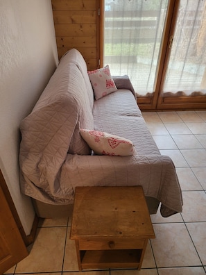 A wooden-framed room with a beige sofa, a small wooden table, and a window with a view of greenery. - 3-star apartment at the base of the slopes, large terrace, 2 bedrooms (Les Deux Alpes)