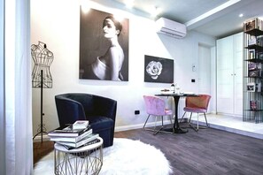 Un interior moderno con piso de madera oscura, una mesa redonda con sillas, un tapete blanco y mullido, y obras de arte en las paredes.